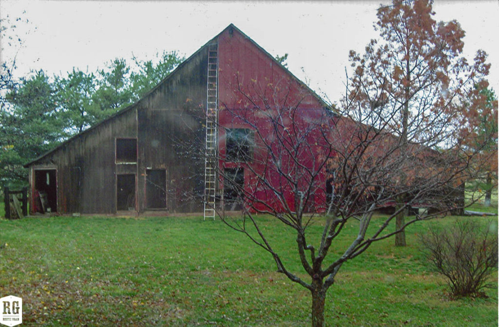 Brown and red barn with peaked roof. A tree with autumn leaves in the foreground.